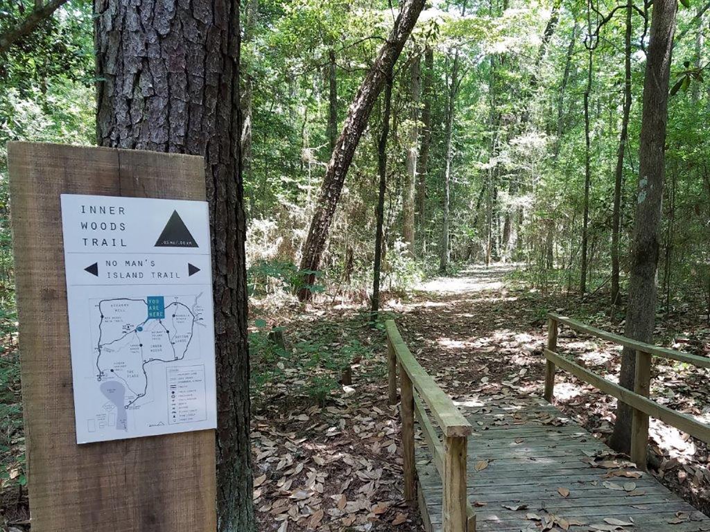 A wooden sign marking the Inner Woods Trail and No Man's Island Trail alongside a path in a lush, green forest.
